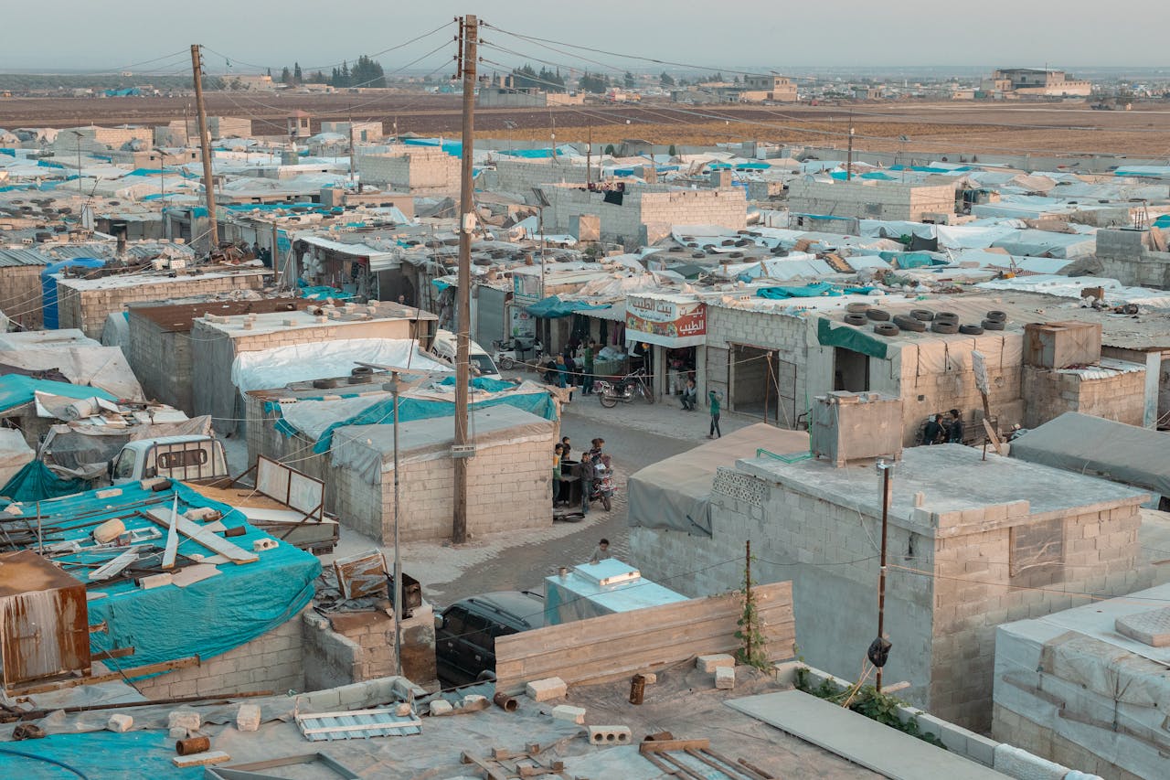 services-01 A broad aerial view of a refugee camp with makeshift shelters and blue tarps in an urban area.