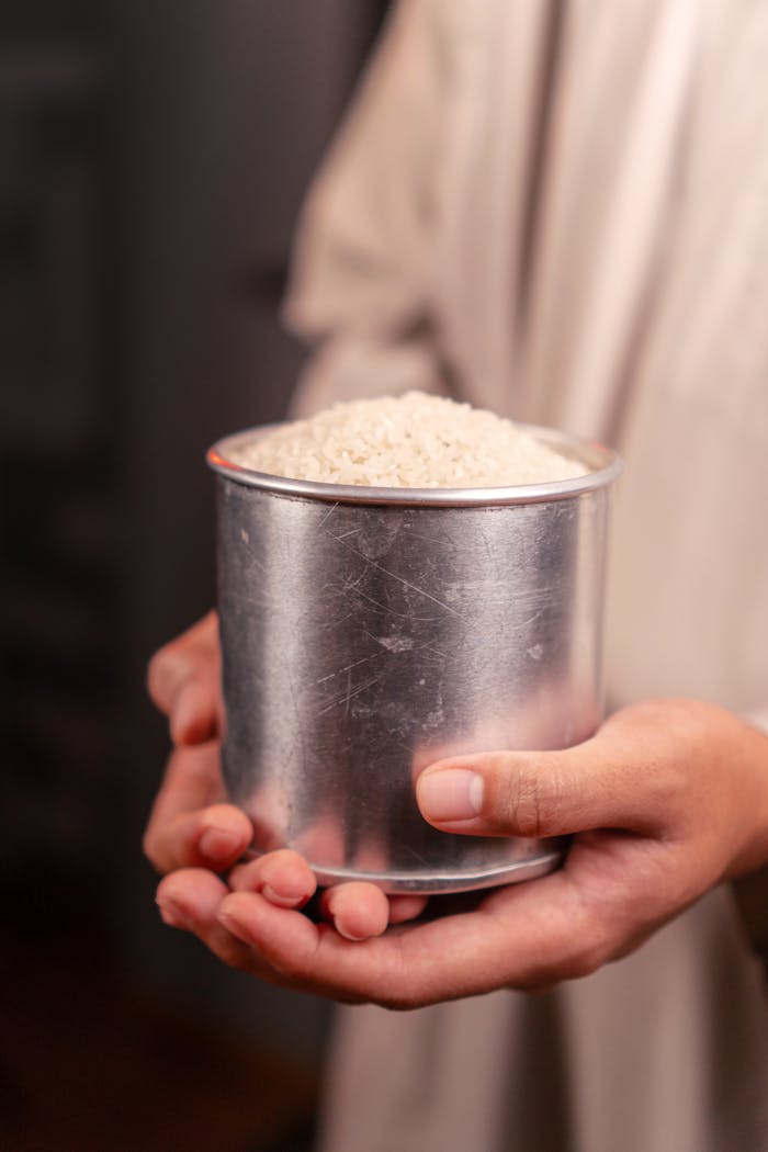 about-us Close-up of hands holding a tin cup full of uncooked white rice, symbolizing abundance.